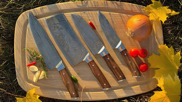 Set of knives on a wooden cutting board with vegetables, surrounded by autumn leaves.