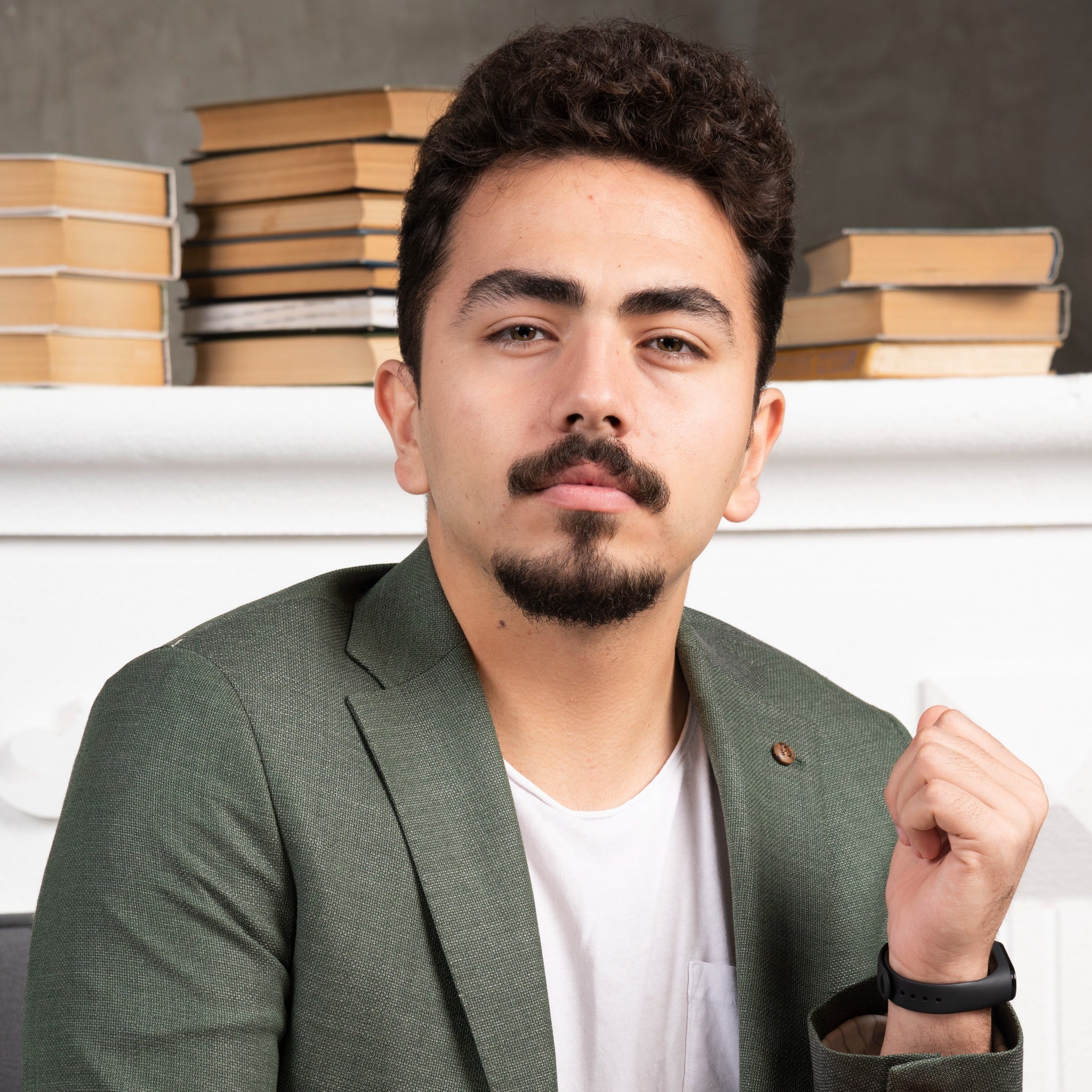 Man in a green blazer sitting in front of stacked books